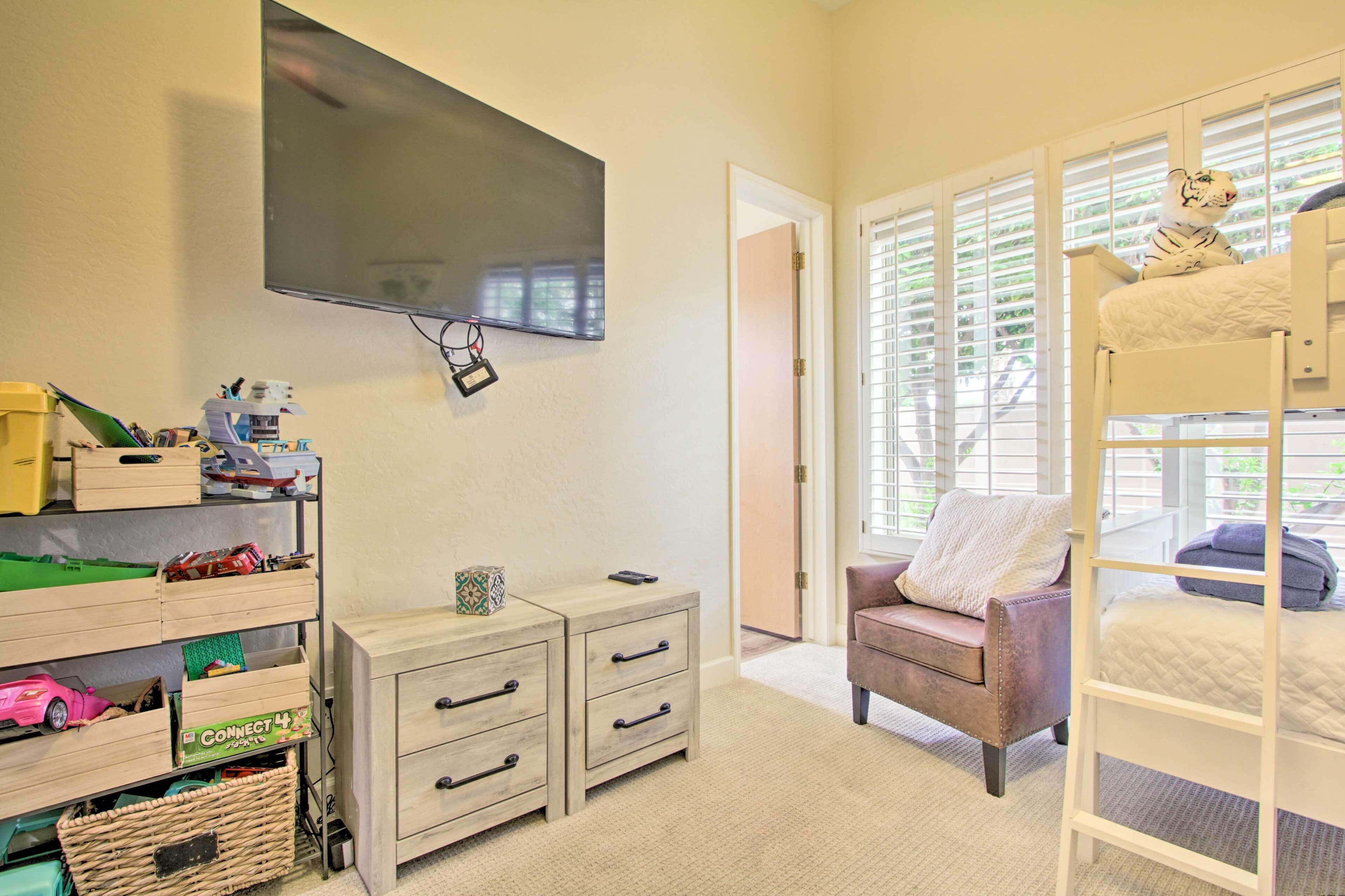 A child's room with a bunk bed, a television, a desk with drawers, and a window with blinds.