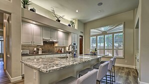 A modern kitchen with a large island, bar stools, and a view of the outdoors through a window with blinds. - Patio, Playground! Glendale Family Gem Near Golf (Glendale)