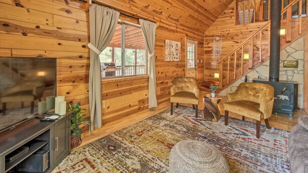 A cozy log cabin interior with a TV, comfortable seating, a fireplace, and a staircase. - Large Deck, Grill: Pet-friendly Show Low Retreat! (Show Low)