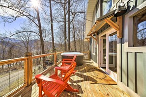 A wooden deck with red Adirondack chairs, a hot tub, and a view of the surrounding forest.