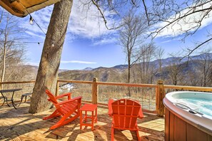 A wooden deck with a hot tub, red Adirondack chairs, and a table.