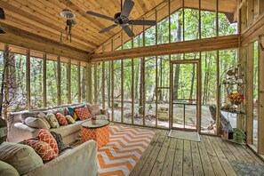 Eine Holzterrasse mit einer Sitzecke, großen Fenstern und einem Deckenventilator.