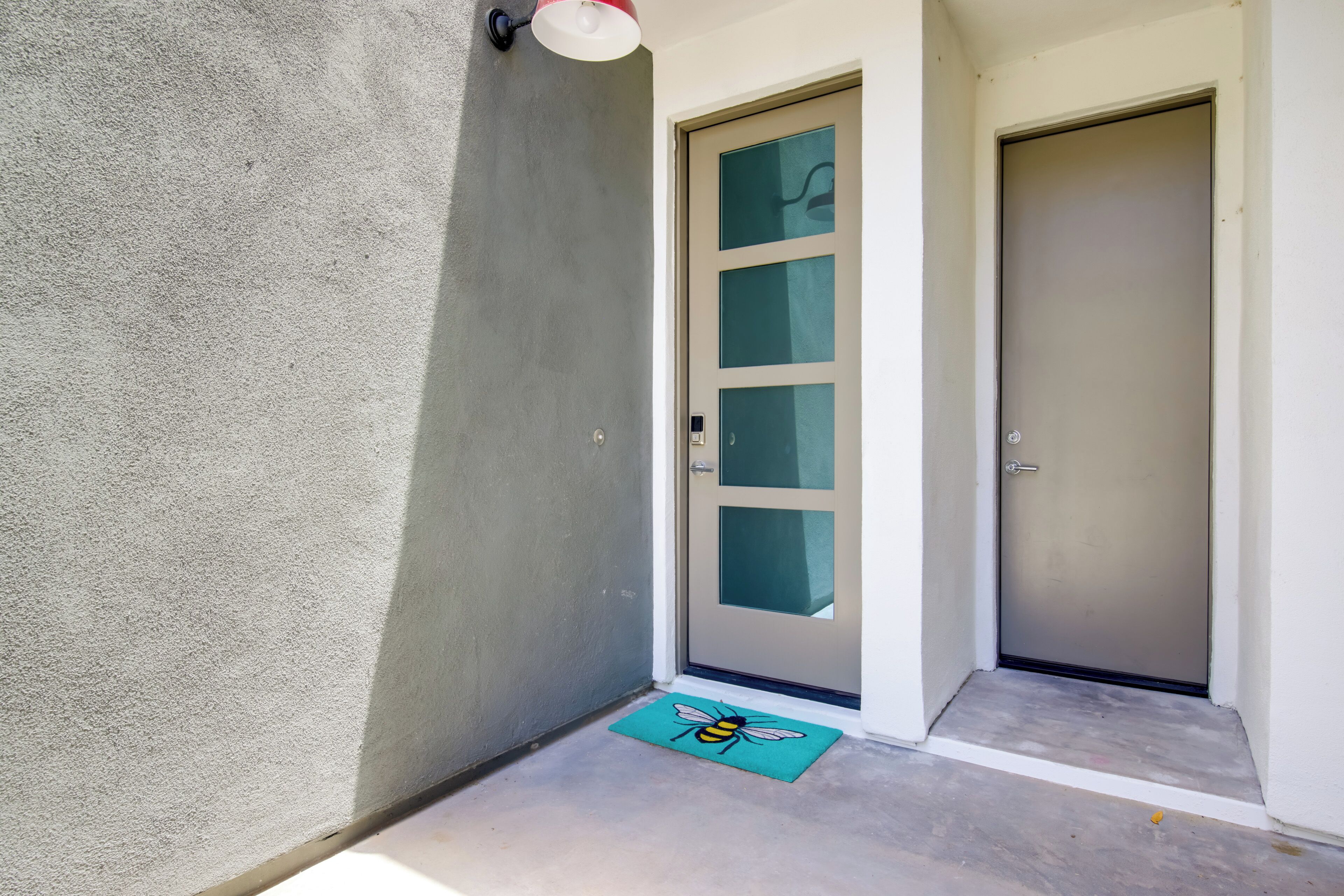 A hallway with a textured wall, a door with frosted glass panels, and a doormat with a bee design.
