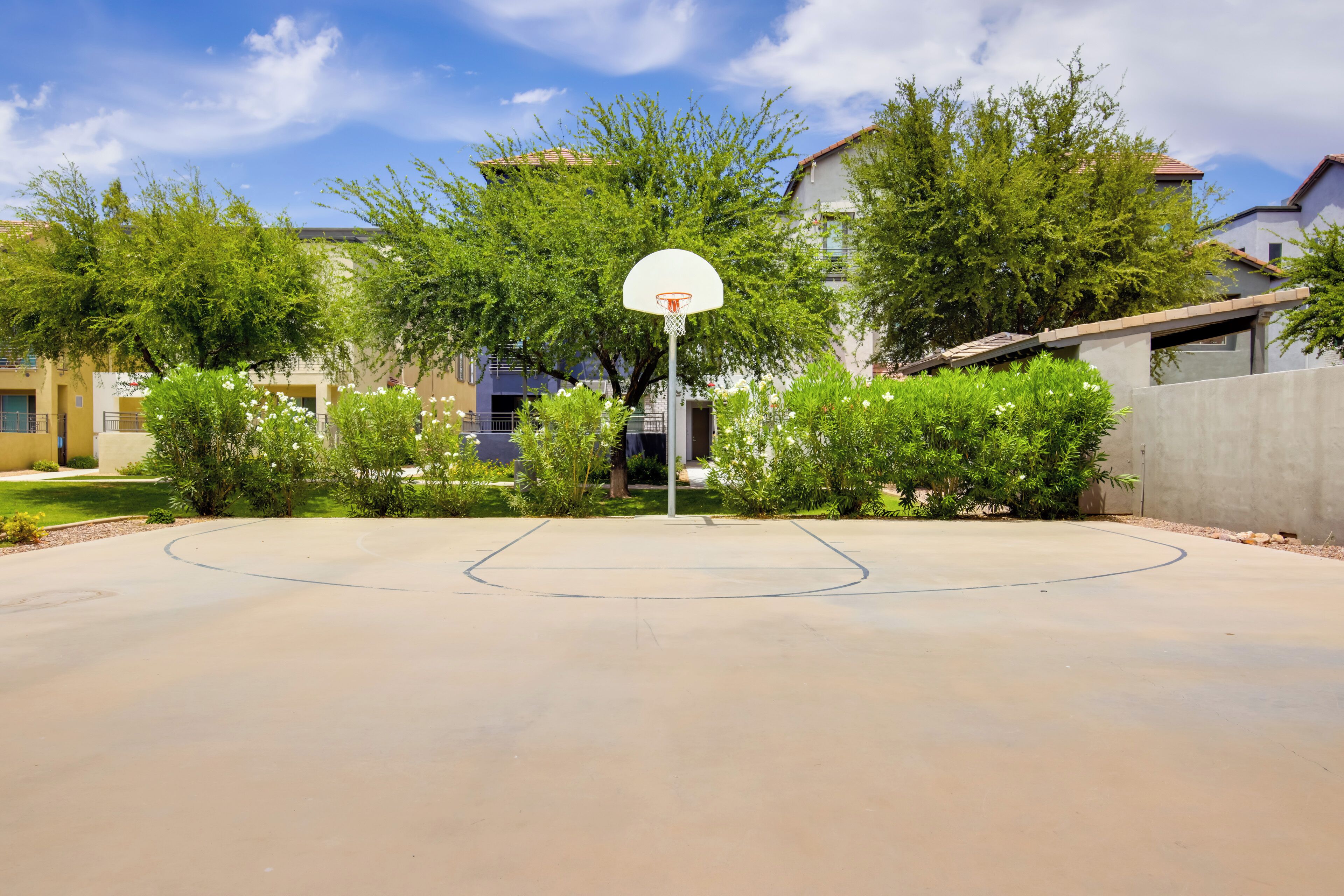 Un terrain de basket en plein air, doté d’un panier, entouré de verdure et de bâtiments résidentiels.