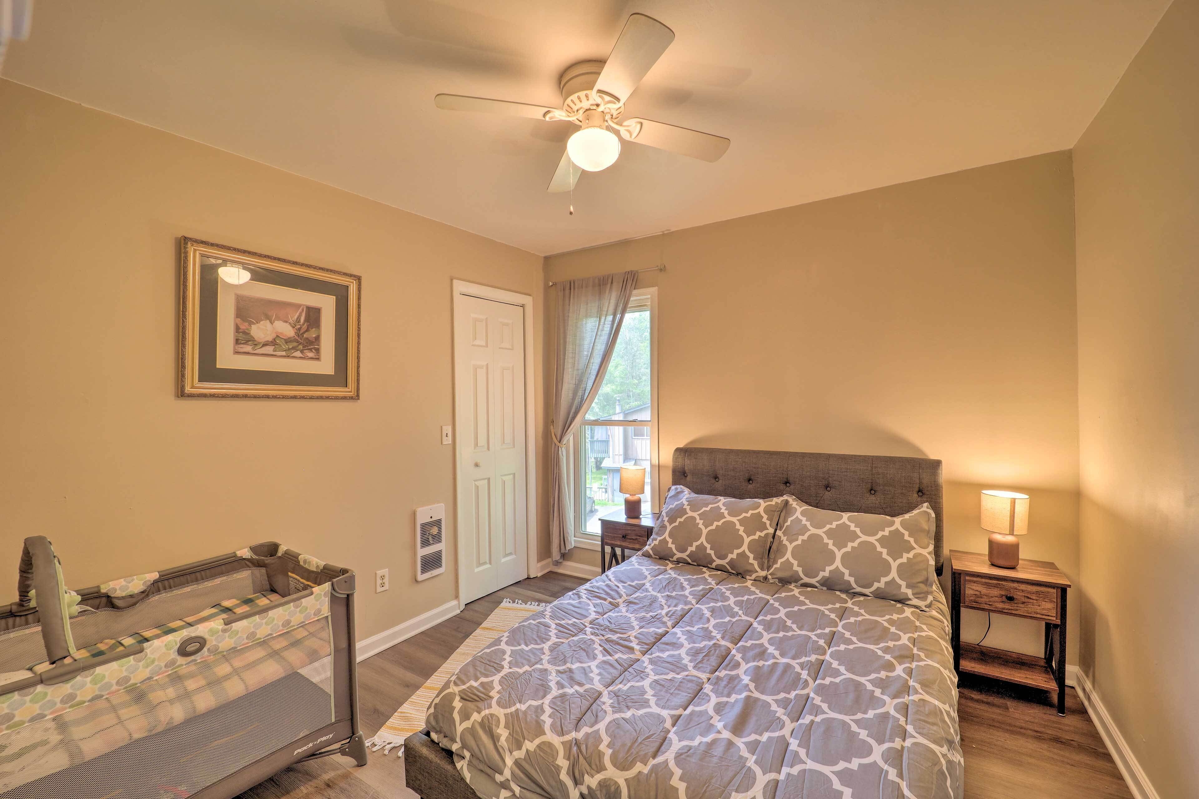 A bedroom with a bed, a nightstand, a ceiling fan, a window with curtains, and a framed picture on the wall.
