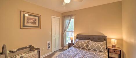 A bedroom with a bed, a nightstand, a ceiling fan, a window with curtains, and a framed picture on the wall.