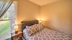 Une chambre à coucher avec un lit, une table de chevet avec une lampe, une fenêtre avec des rideaux et une prise électrique au mur.