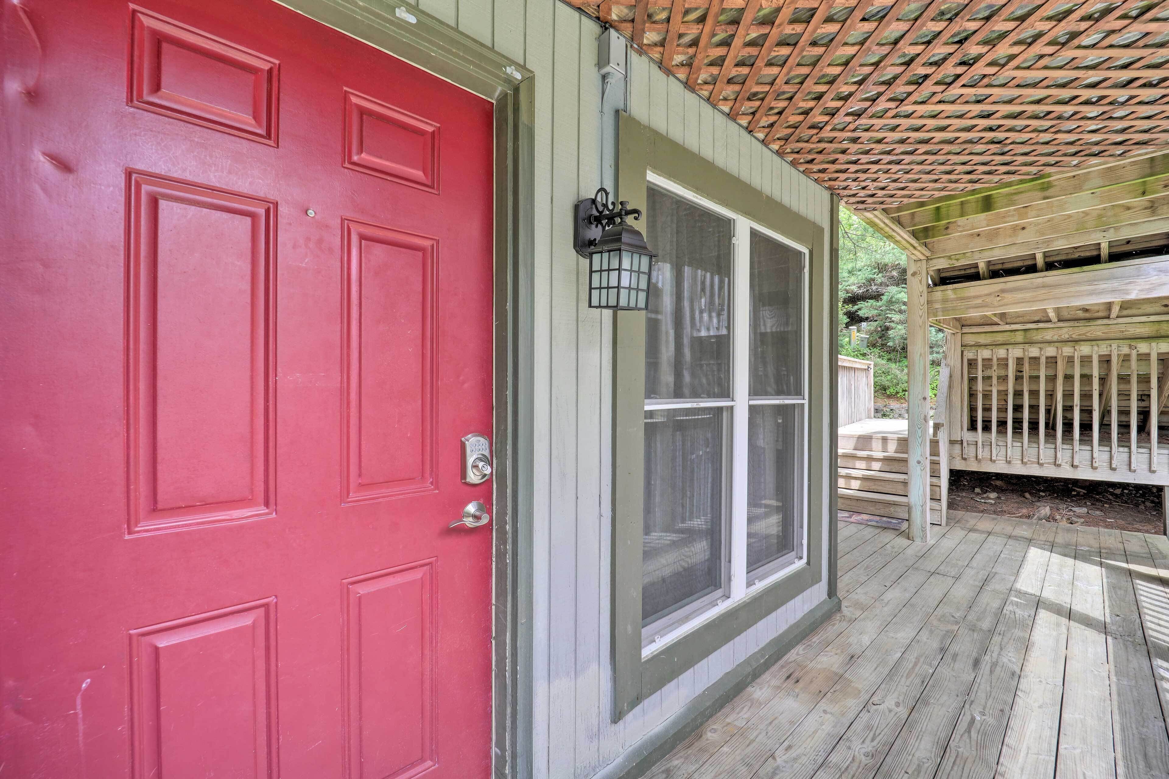A red door with a window, a wooden deck, and a pergola.