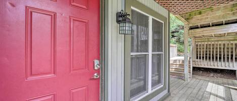 A red door with a window, a wooden deck, and a pergola.
