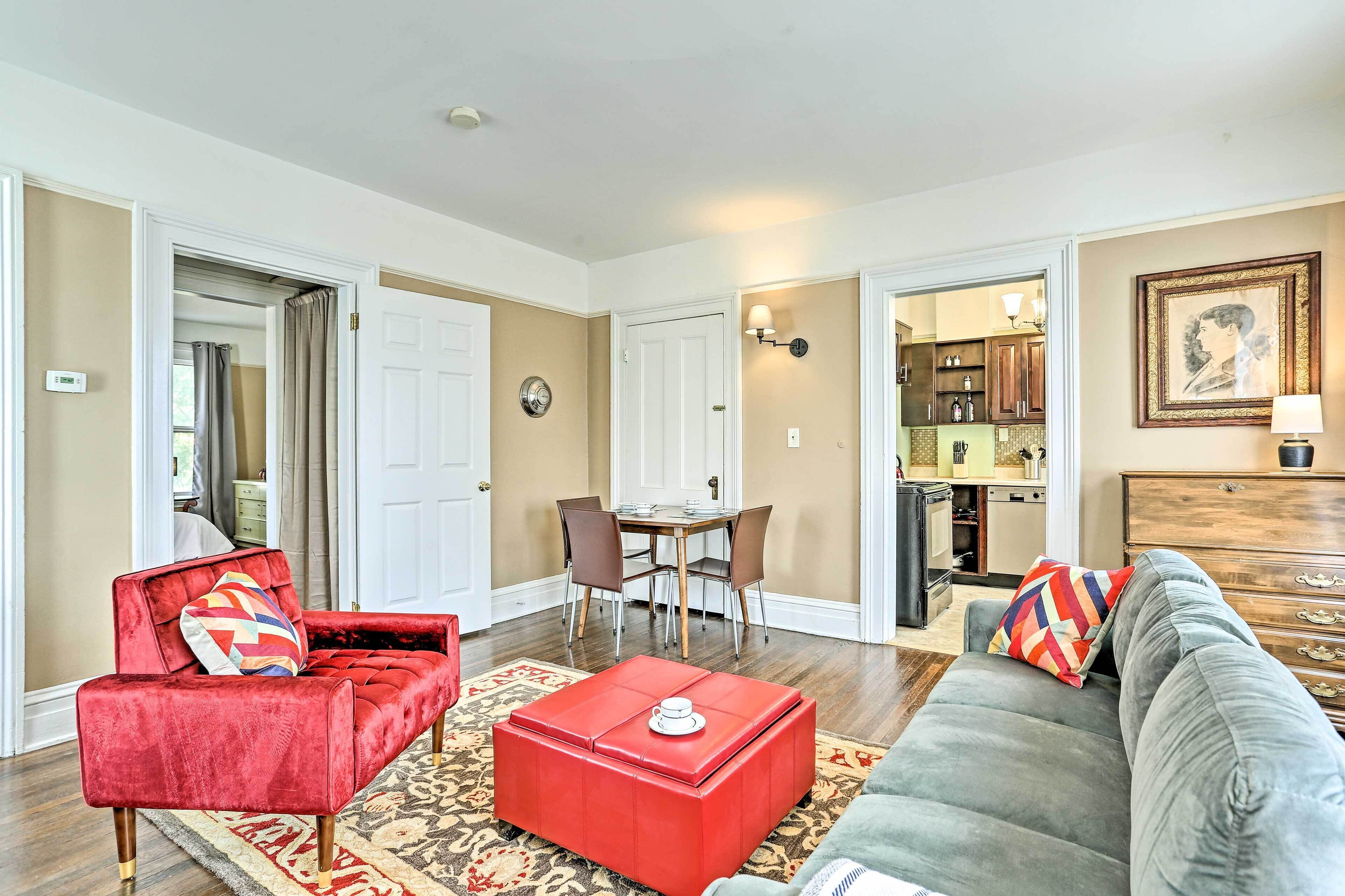 A living room with a red sofa, a grey couch, and a red ottoman. There is a dining area with a table and chairs.