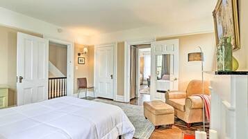 A bedroom with a large bed, a chair, a small table, and a staircase leading to another room.