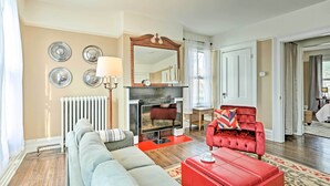 Ein Wohnzimmer mit Kamin, einer Couch, einem roten Sessel und einem roten Hocker.