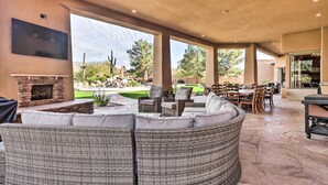 A covered outdoor living area with a stone fireplace, wicker furniture, and a flat-screen TV mounted on the wall. - Lavish Estate w/ Sports Court & Home Theater! (Scottsdale)