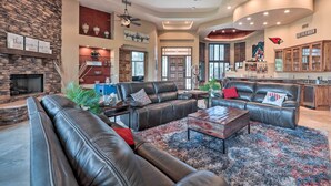 A spacious living room with leather sofas, a fireplace, ceiling fans, and a kitchen area with cabinets and a sign for 'Ice Cold Beer'. - Lavish Estate w/ Sports Court & Home Theater! (Scottsdale)