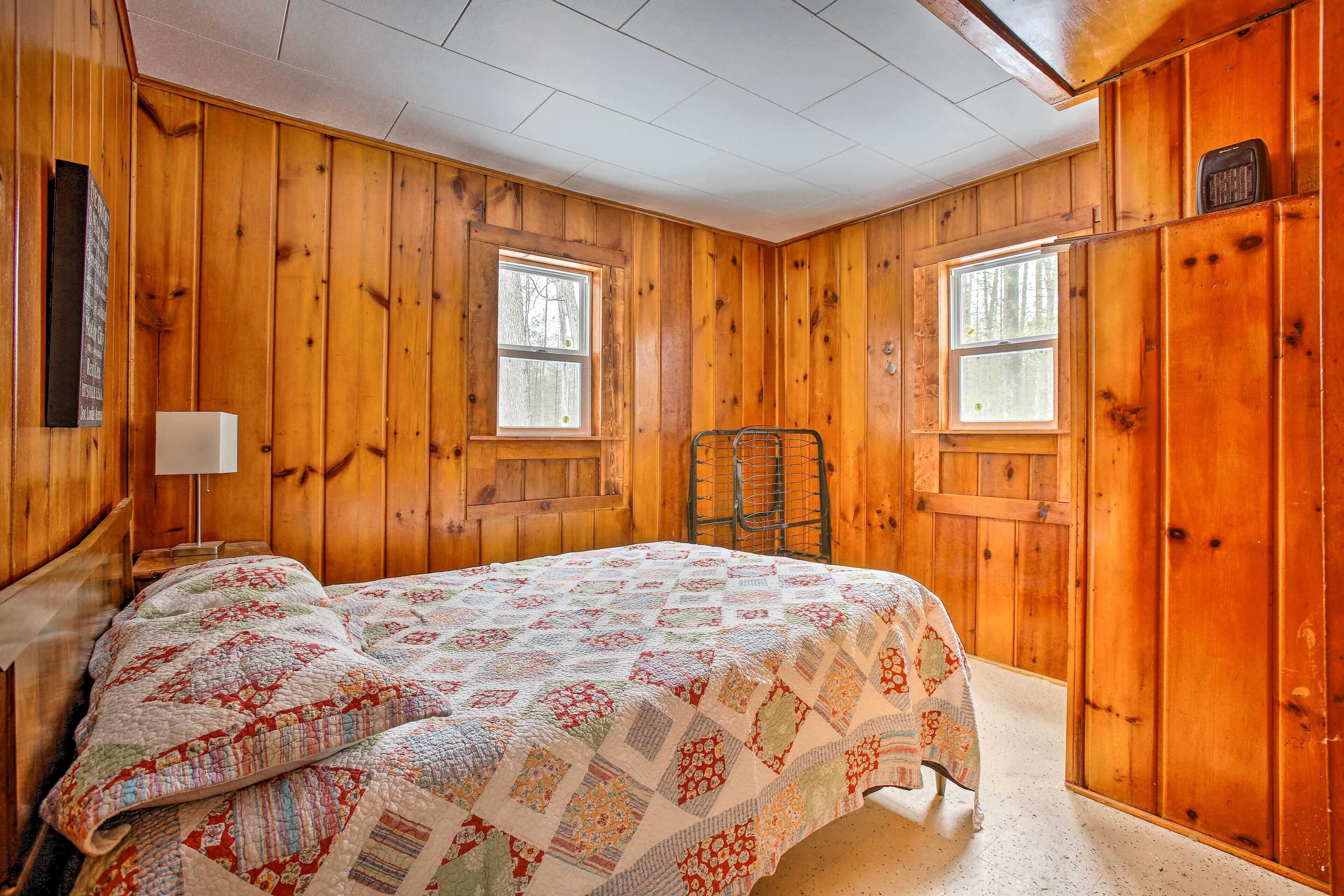 Un dormitorio con paneles de madera, una cama, dos ventanas y una silla.