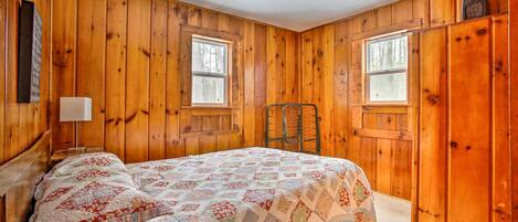 Un dormitorio con paneles de madera, una cama, dos ventanas y una silla.