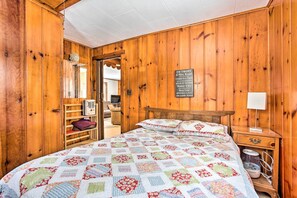Ein Zimmer mit Holzwänden, einem Bett, einem Nachttisch, einer Lampe und einem Schild mit Auflistung benachbarter Orte.