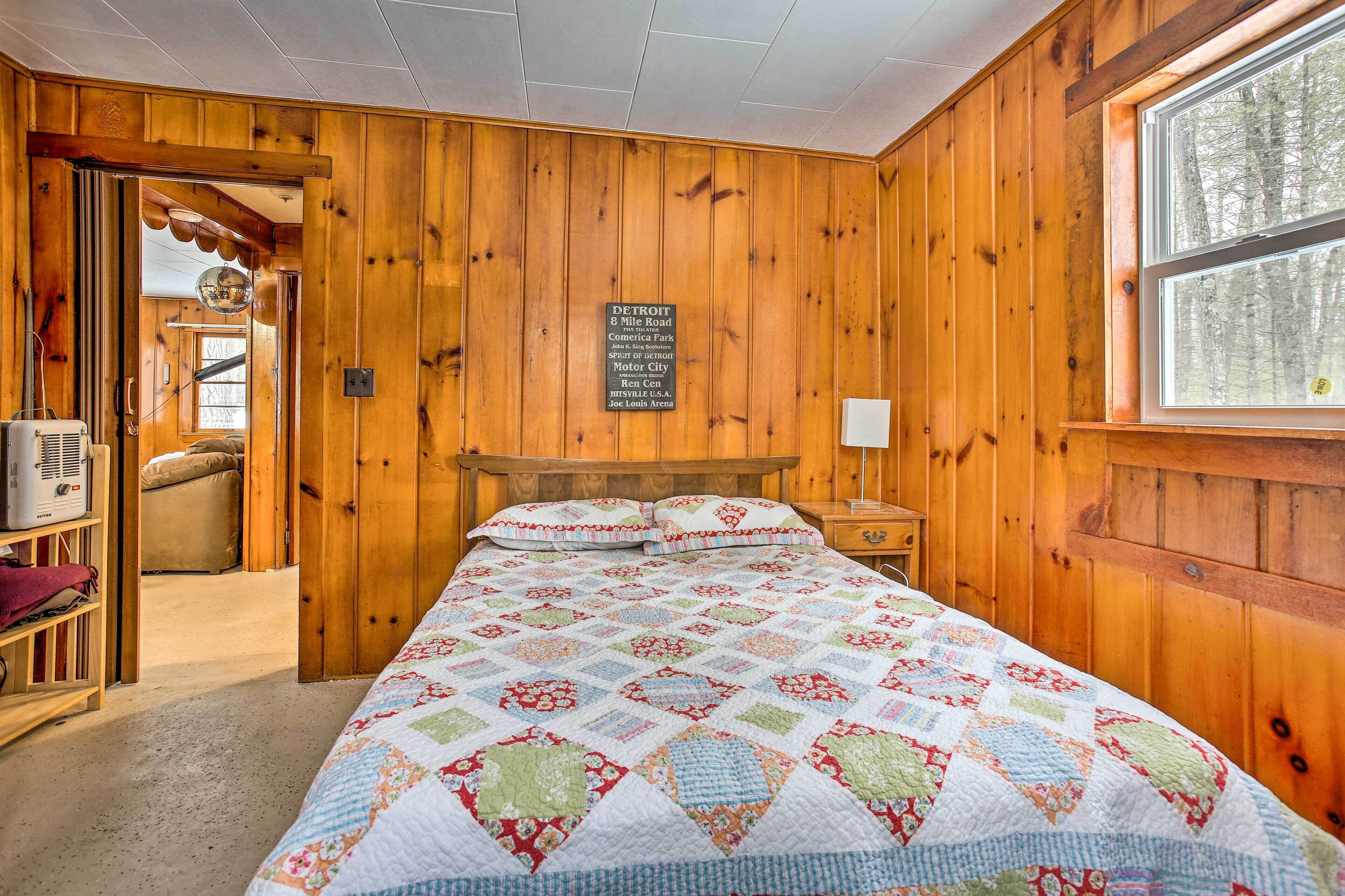 A wooden-paneled bedroom with a quilted bedspread, a sign indicating the location, and a window with a view of trees.