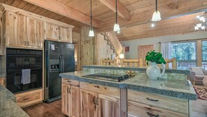 Une cuisine avec des meubles en bois, un réfrigérateur noir, un four encastré, des plans de travail en granit et des luminaires suspendus.