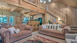 Un vaste espace de vie comprenant deux canapés en cuir, un tapis à motifs et un escalier menant à un niveau supérieur.