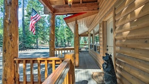 Une cabane en bois avec un porche, une statue d’ours et un drapeau américain.
