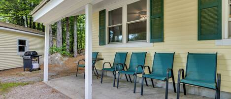 A covered porch with green chairs and a grill.