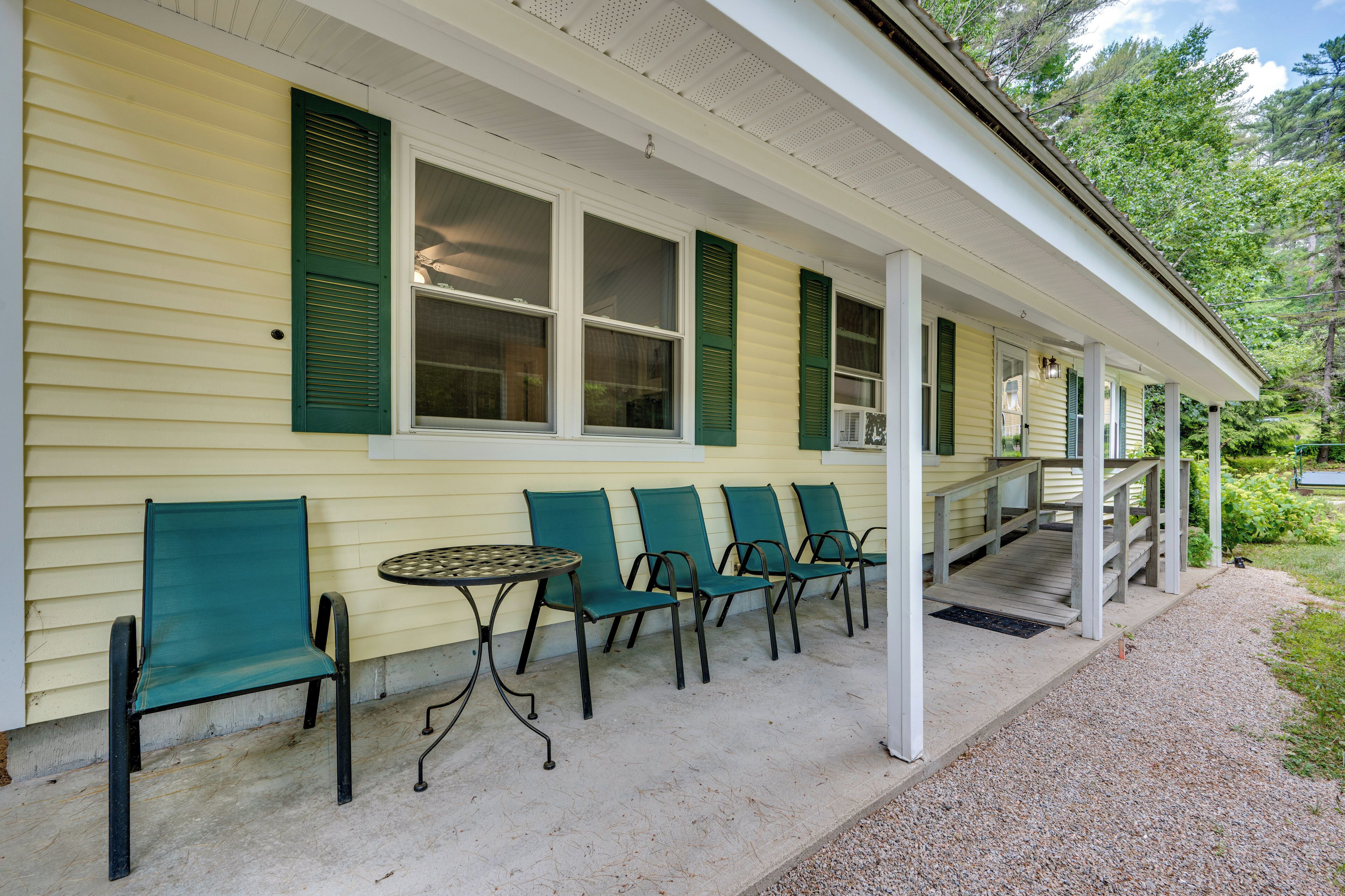 Eine Veranda mit grünen Stühlen und einem kleinen Tisch, ein überdachter Gang und ein Haus mit gelben Wandverkleidungen und grünen Fensterläden.