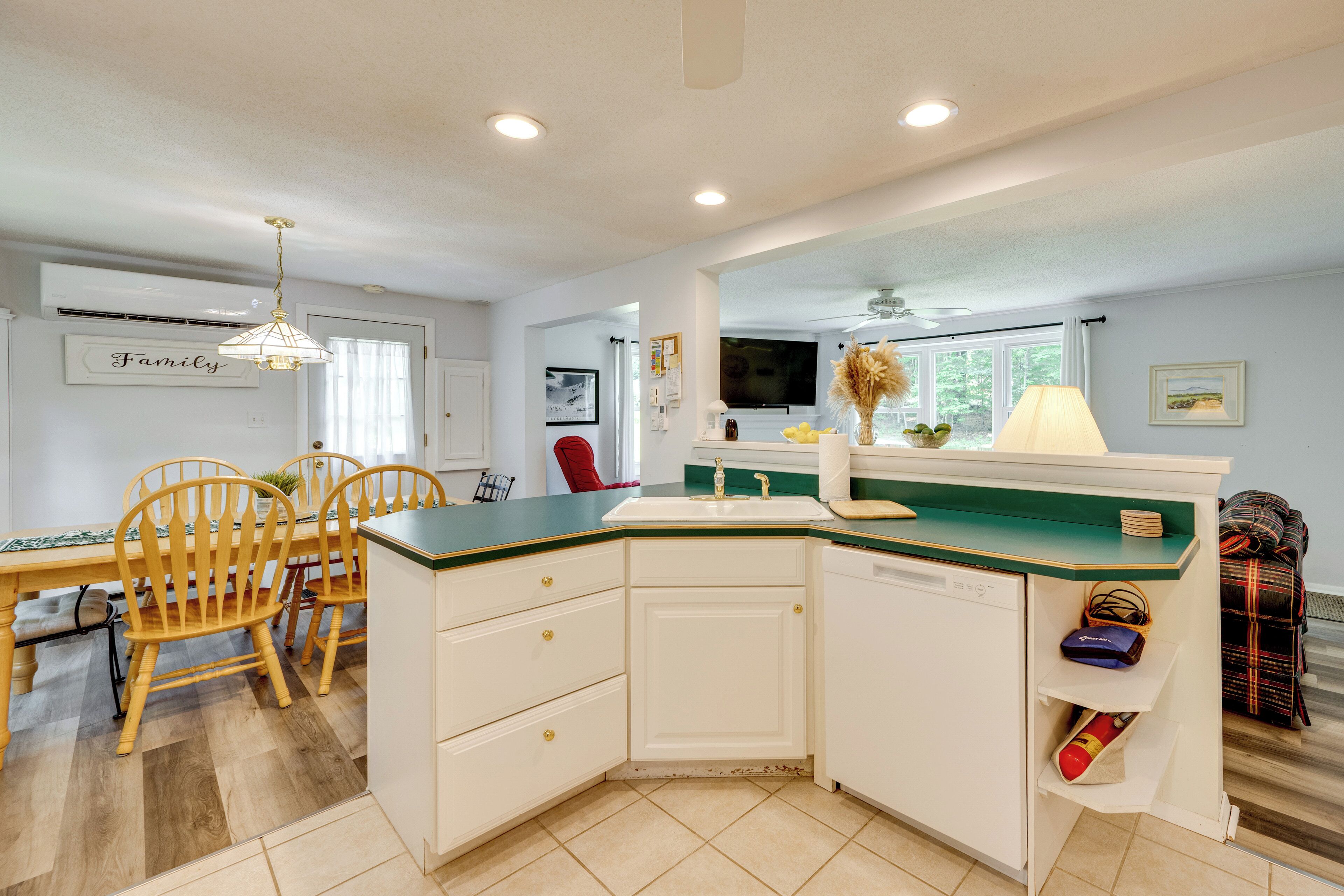 A kitchen with white cabinets, a green countertop, and a dining area with wooden chairs.