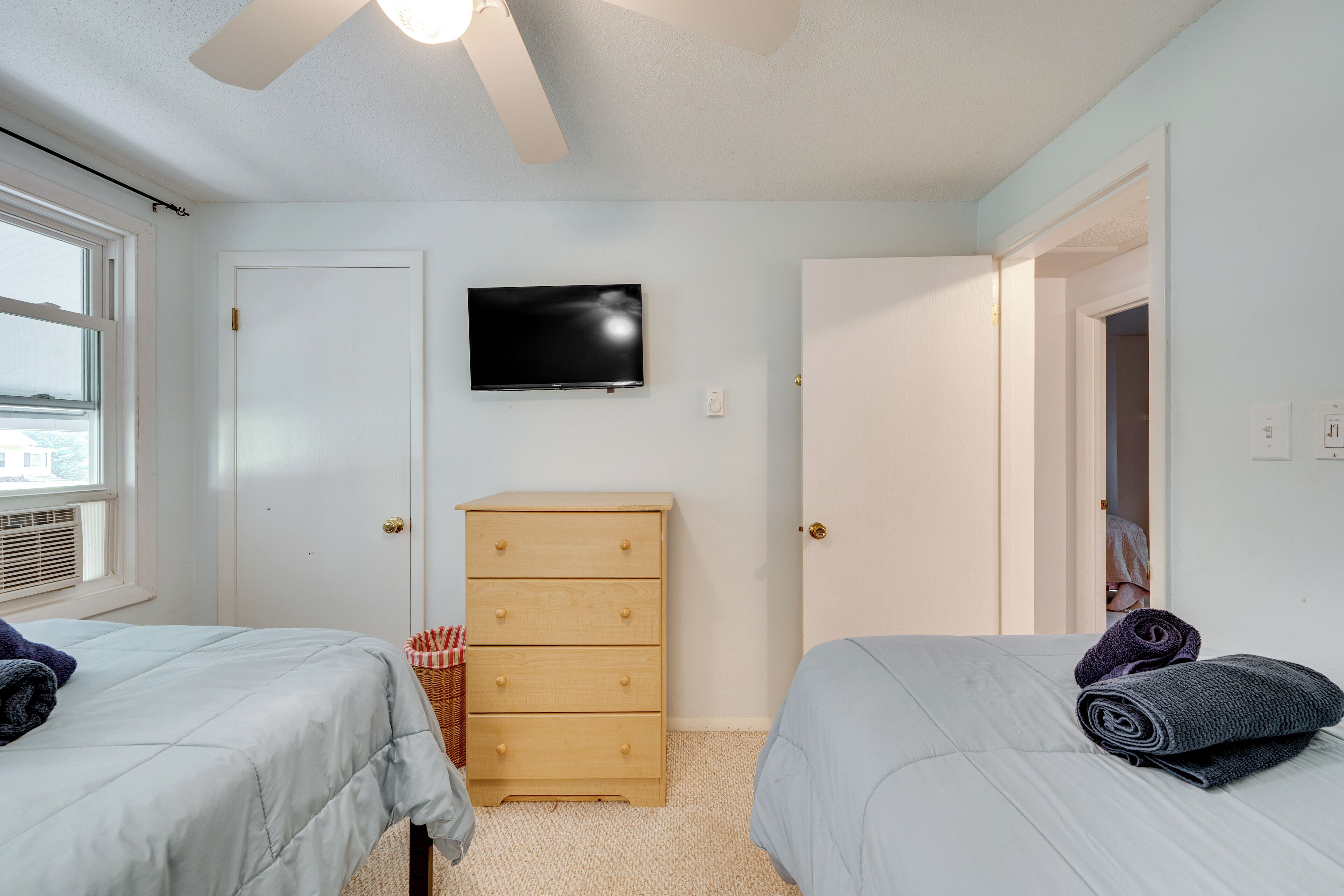 A bedroom with two beds, a TV, a dresser, and a window.