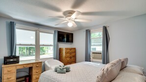 Une chambre à coucher comprenant un lit, un bureau, une chaise, un téléviseur et un ventilateur de plafond.