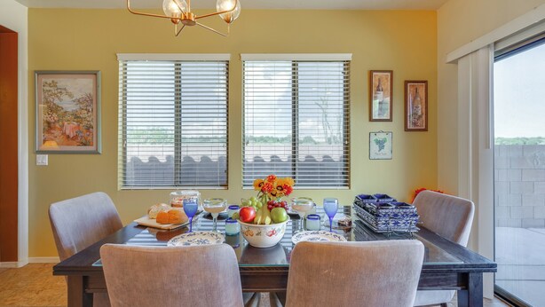 A dining area with a table set for four, featuring a fruit bowl, glasses, and a decorative centerpiece. - Step-free Sahuarita Retreat! Patio + Pool Access (Sahuarita)