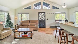 A spacious living room with a high ceiling, a wooden ceiling fan, a large window, a brown leather sofa, a wooden coffee table, and a small Christmas tree. - Near Hiking: Modern Heber-overgaard Cabin w/ Deck (Overgaard)