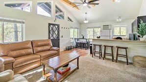A spacious living area with a brown leather sofa, a wooden coffee table, and a kitchen with a bar area. - Near Hiking: Modern Heber-overgaard Cabin w/ Deck (Overgaard)