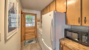 A kitchen with wooden cabinets, a white refrigerator, a microwave, and a door leading outside. - Lakefront Home With Deck, Dock, & Water Access! (Liberty)