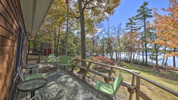 A covered patio with green chairs and tables, overlooking a lake with autumn foliage. - Lakefront Home With Deck, Dock, & Water Access! (Liberty)