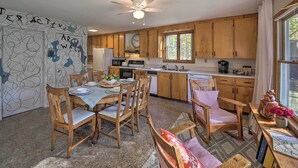 A kitchen with wooden cabinets, a dining table with chairs, a ceiling fan, and a window with curtains. - Lakefront Home With Deck, Dock, & Water Access! (Liberty)