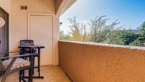 Un balcon avec une table ronde et des chaises, une porte et une vue sur les arbres et les bâtiments.