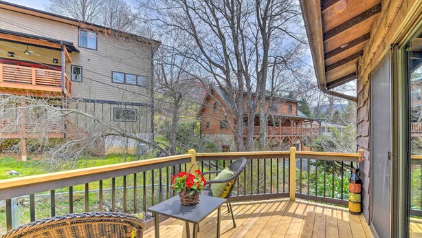 Une terrasse en bois avec une chaise en osier et une table, un panier de fleurs et une vue sur les maisons voisines.