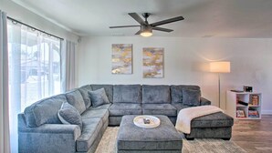 A modern living room with a sectional sofa, a ceiling fan, and artwork on the walls.