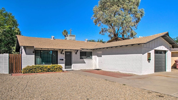 A single-story house with a white exterior, a front porch, and a gravel driveway.