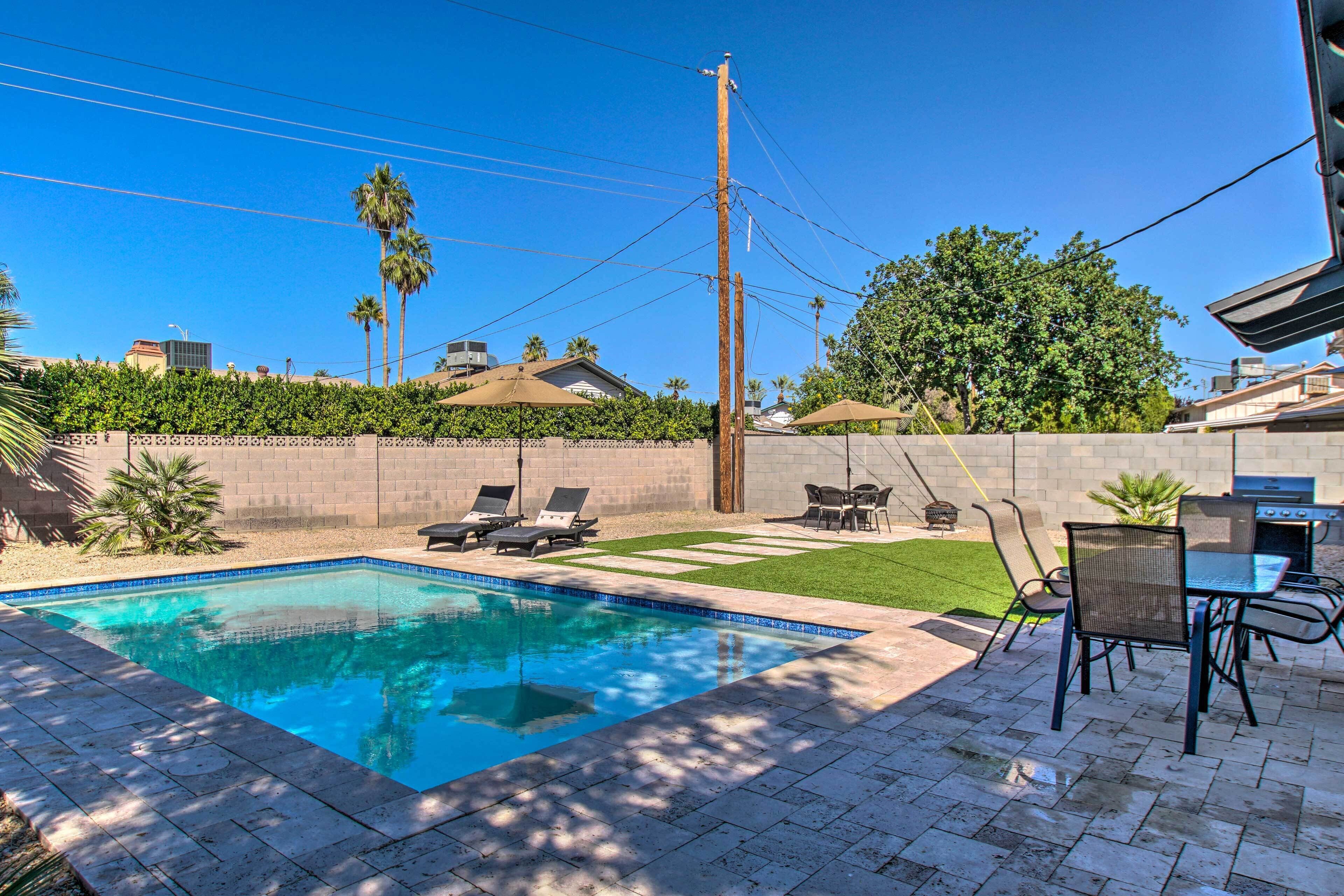 A swimming pool with lounge chairs, a barbecue grill, and a patio area with a table and chairs.