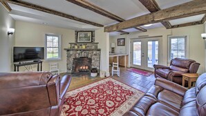 A spacious living room with leather sofas, a stone fireplace, and a large window. - Riverfront Coastal Escape With Deep Water Dock! (Wiscasset)
