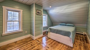 A bedroom with a sloped ceiling, wooden flooring, and a bed with a green bedspread. - Riverfront Coastal Escape With Deep Water Dock! (Wiscasset)