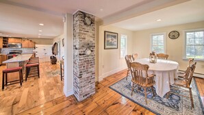 A spacious kitchen with wooden flooring, a brick column, and a dining area with a round table and wooden chairs. - Riverfront Coastal Escape With Deep Water Dock! (Wiscasset)