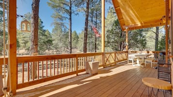 A wooden deck with a railing, tables, and chairs.