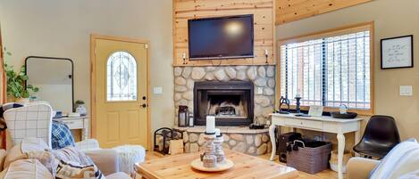 A cozy living room with a stone fireplace, wooden ceiling, and a flat-screen TV mounted above it.