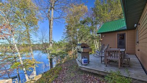 A cabin with a deck, a grill, and a view of a lake. - Powell Lake 'UP Badger Lodge Bnb' w/ Shared Dock (Wetmore)