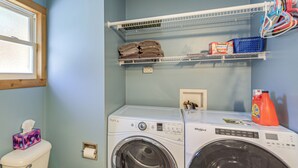 A laundry area with two front-loading washing machines, a shelf with folded towels, and a toilet with a tissue box. - Powell Lake 'UP Badger Lodge Bnb' w/ Shared Dock (Wetmore)