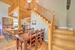 A spacious kitchen with wooden cabinets, a dining area with a large wooden table and chairs, and a wooden staircase leading to an upper level.