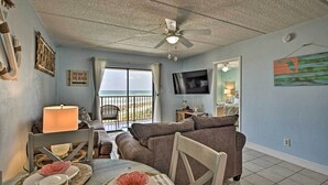 A living room with a view of the beach, a ceiling fan, a TV, and a dining area with a table and chairs. - Oceanfront Ormond Beach Getaway w/ Balcony! (Ormond Beach)
